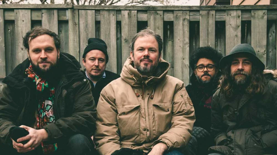 Five men sitting outdoors in front of a wooden fence